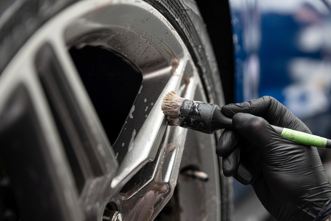 Car detailing studio worker cleaning car wheel